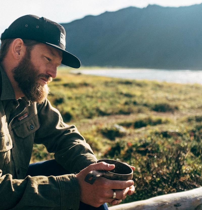 Hombre con una taza Kupilka a orillas de un lago en el norte de Finlandia
