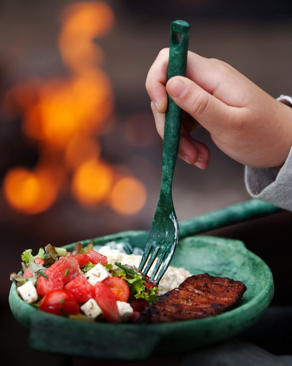 Plato Kupilka verde con ensalada y un tenedor, con fogata de fondo